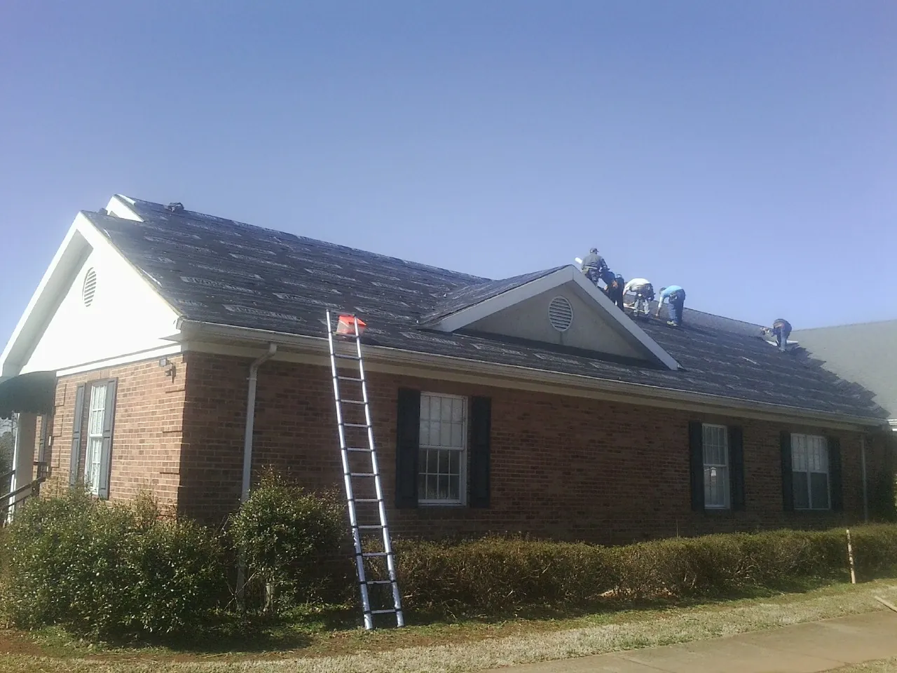 Crew tearing shingles off a brick ranch roof with a ladder set — Emergency Roof Repair work by our crew in Lisbon Falls