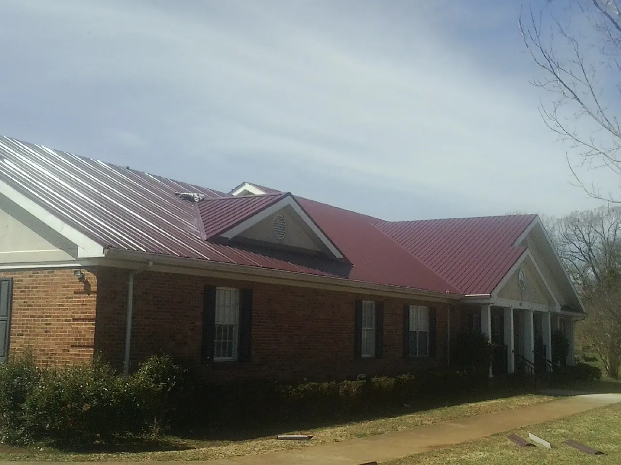 Red metal roof with gabled entries on a long brick building, from a Hail Damage Roof Repair job in Lisbon Falls