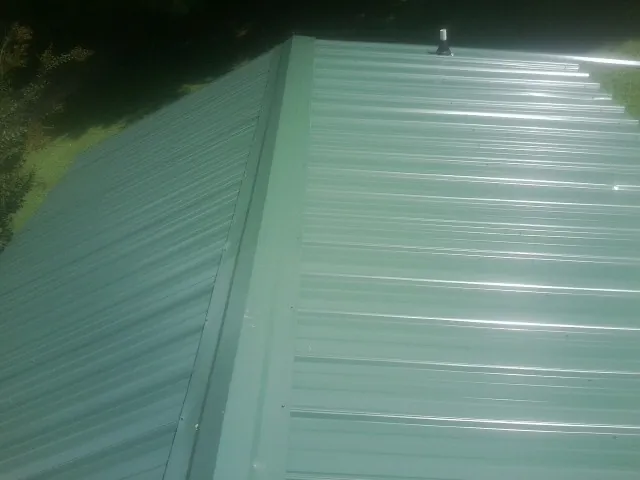 New green metal panels meeting at the ridge of a roof — Flat Roof Repair work by our crew in Lisbon Falls