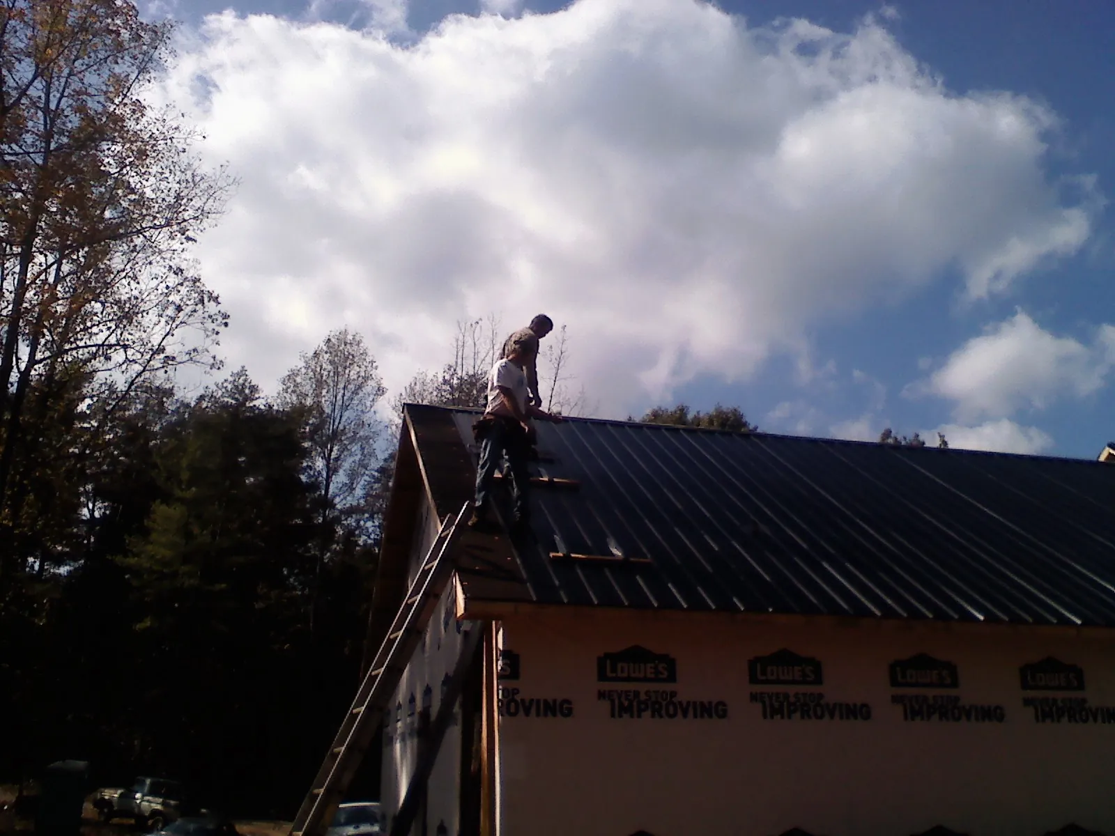 Roofer fastening dark metal panels high against a cloudy sky, from a Roof Inspection job in Lisbon Falls