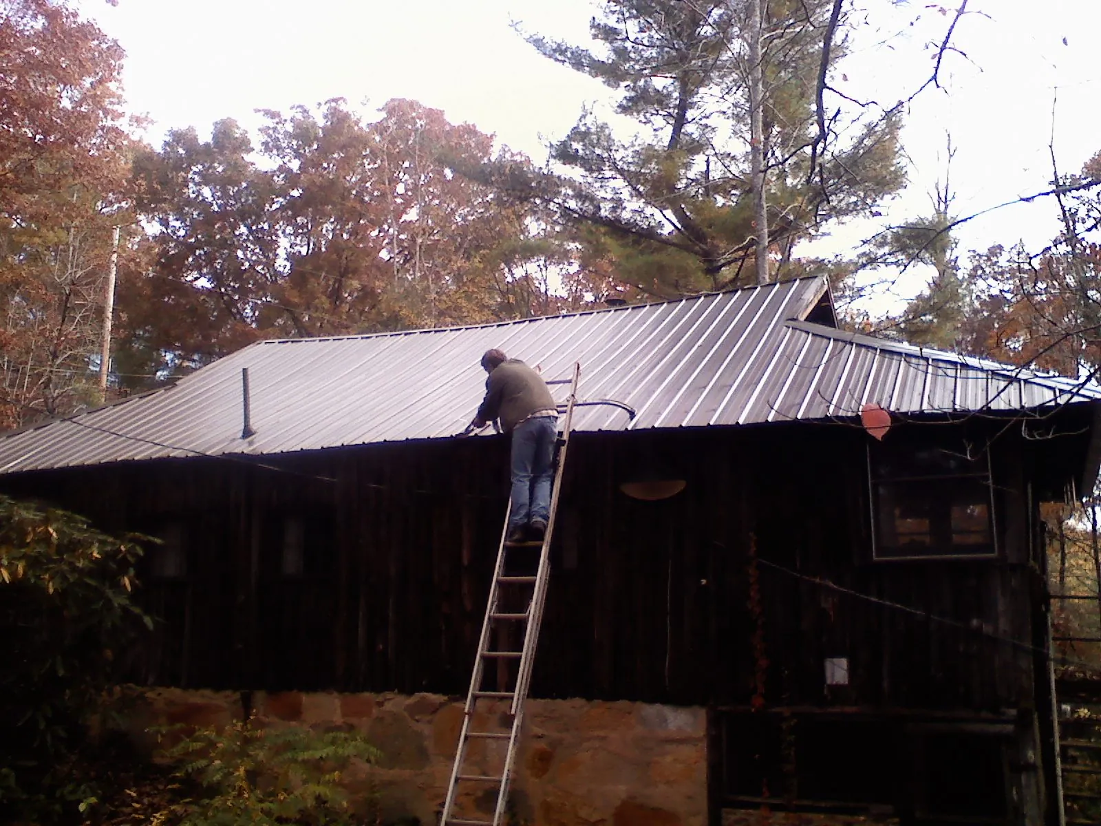 Roofer on a ladder working along the edge of a cabin metal roof in Lisbon Falls