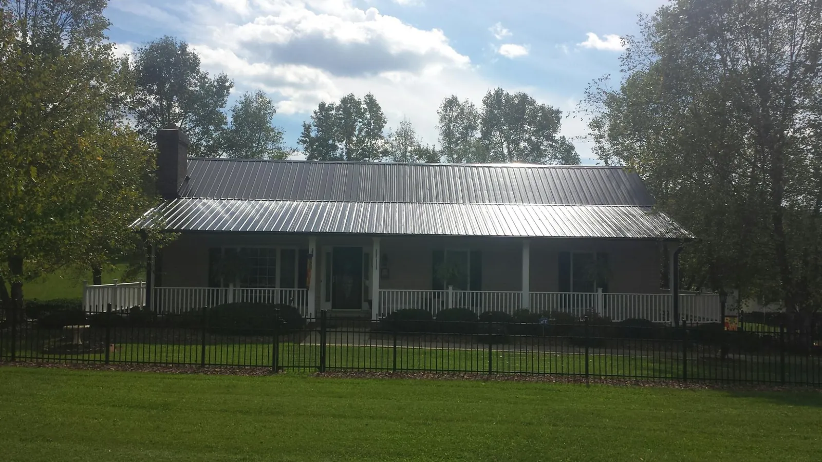 Gray metal roof on a brick ranch with a full width front porch — Gutter Guard Installation work by our crew in Lisbon Falls