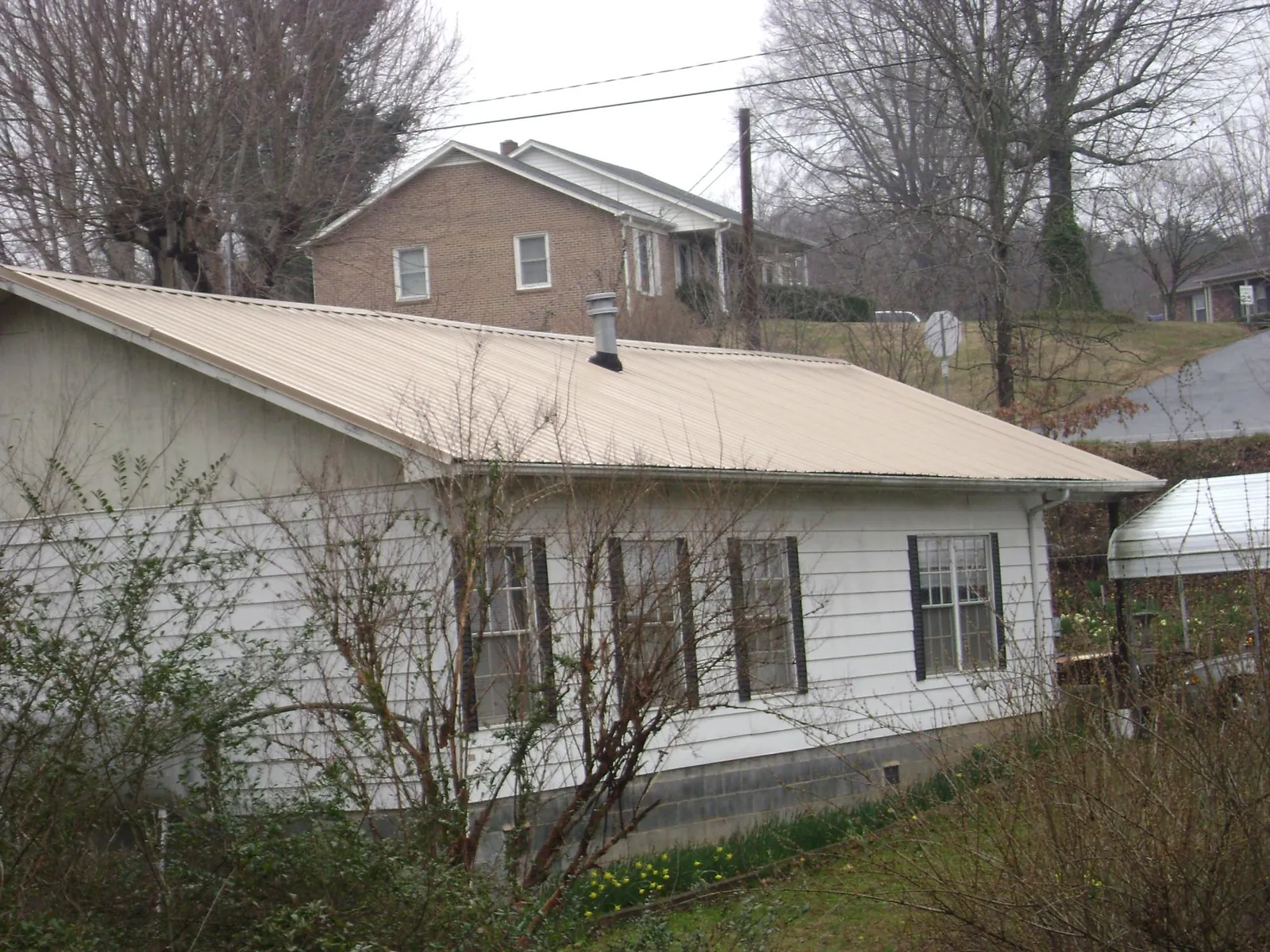 Tan metal roof on a white sided house set into a hillside — Commercial Roofing by Roofing Brothers in Lisbon Falls