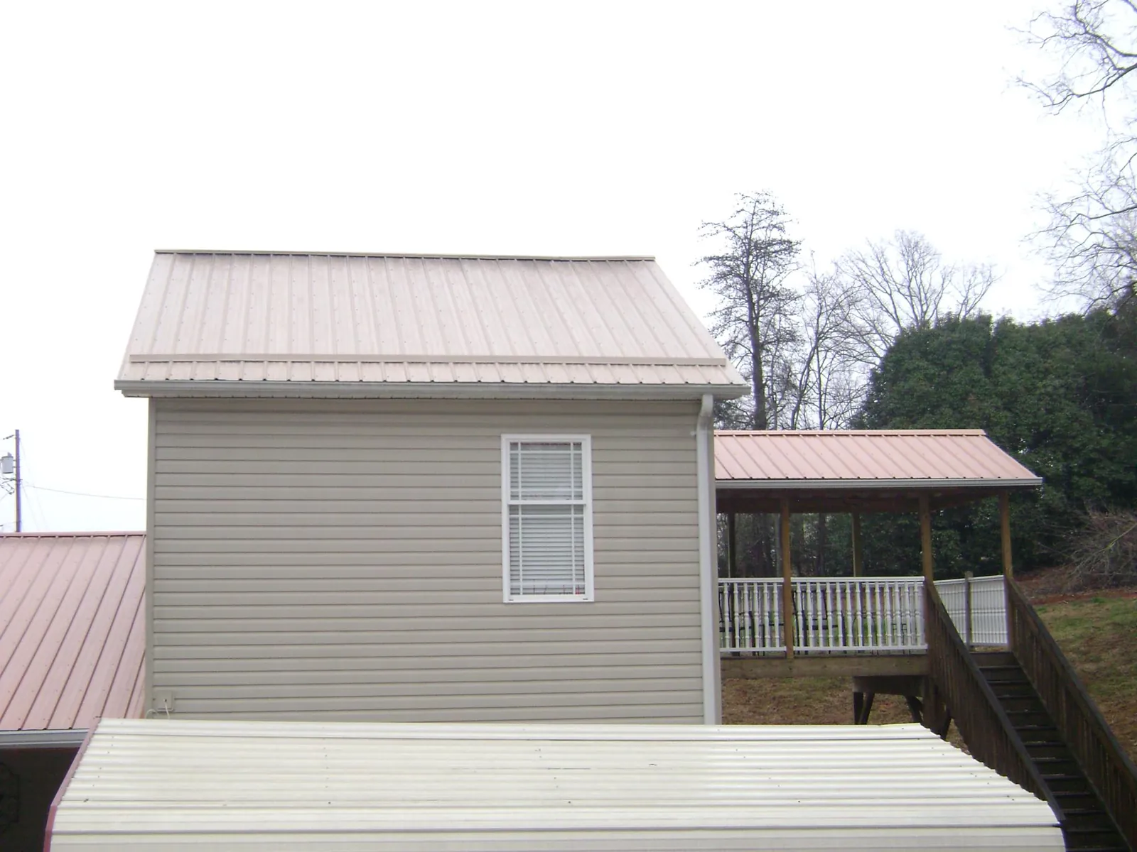 Tan metal roofs on a two story addition and attached porch, from a Roof Replacement job in Lisbon Falls